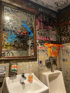 two urinals in a bathroom with graffiti on the walls and above them is a mirror