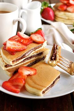 pancakes with strawberries and chocolate filling on a white plate next to two cups of coffee