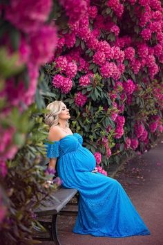 a pregnant woman in a blue dress sitting on a bench with pink flowers behind her