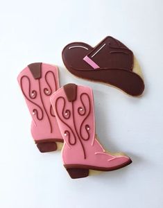 two decorated cookies with cowboy boots and a pink hat on them, one has chocolate icing