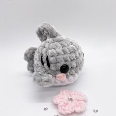 a small crocheted gray and pink teddy bear next to a tiny white flower