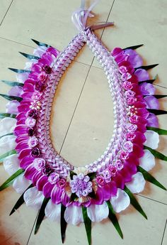 a purple and white necklace with flowers on the bottom is hanging from a string in front of a tile floor