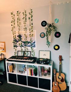 a room with various musical instruments and plants hanging on the wall above it is a white shelf with black bins filled with records