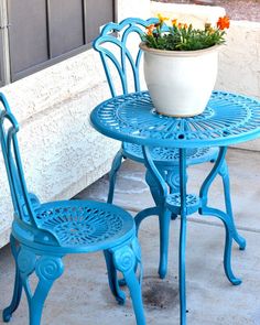 two blue chairs and a table with a potted plant on the top, outside