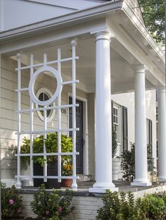 a house with white columns and a clock on the front door, surrounded by plants