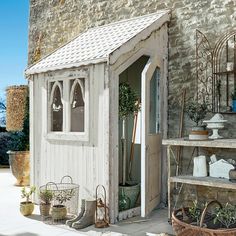 an outdoor storage shed with potted plants and other items on the shelves in front of it