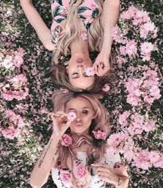 two women laying on top of each other in front of pink flowers and greenery