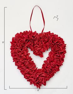 a red heart shaped decoration hanging on a white wall next to a measuring tape and ruler