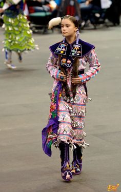 a woman in an elaborately decorated dress walks down the street with other people behind her