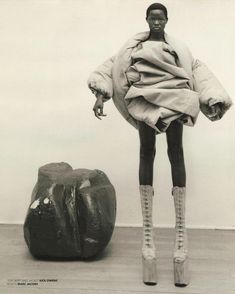 a black and white photo of a woman standing next to a rock