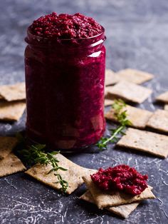 a glass jar filled with red beet sauce next to crackers on a table