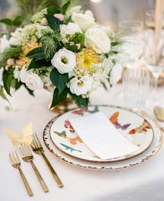 the table is set with white flowers and gold place settings