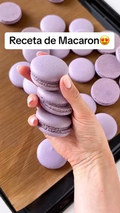 a person holding a purple macaron in front of a wooden board with other macarons on it