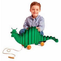 a young boy sitting on the ground playing with a green wooden toy lizard that is shaped like a house