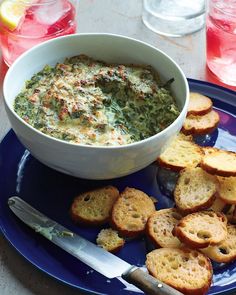 a blue plate topped with bread slices and a bowl of spinach dip next to it