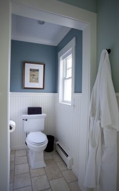 a white toilet sitting next to a window in a bathroom under a painting on the wall