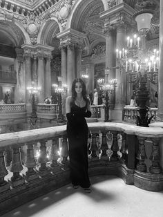 a woman in a long dress standing on a balcony with chandeliers and candles