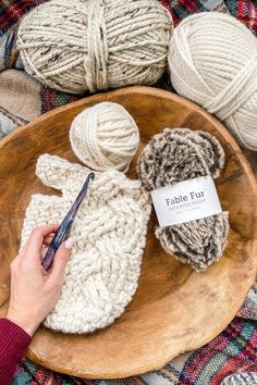 a person holding a crochet hook next to balls of yarn on a wooden platter