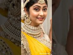 a woman in a yellow and white sari with gold jewelry on her neck is smiling at the camera