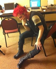 a man with red hair sitting on a chair in front of a desk and computer