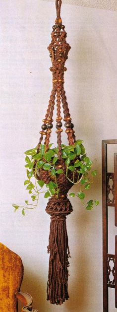 a potted plant hanging from a rope on a wall next to a wooden chair