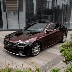 a brown car parked in front of a building on a sidewalk next to some bushes