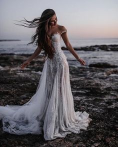 a woman standing on top of a rocky beach next to the ocean wearing a wedding dress