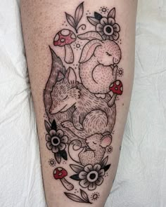 a woman's leg with tattoos on it and flowers around the legs, including an image of two rabbits