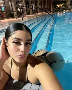 a woman in a bathing suit sitting next to a swimming pool with her hand on her head