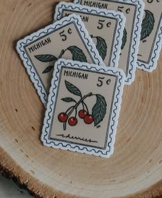 four michigan stamps with cherries on them sitting on a piece of wood in front of a slice of tree