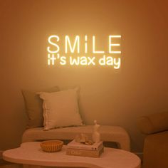 a white couch sitting under a neon smile it's wax day sign