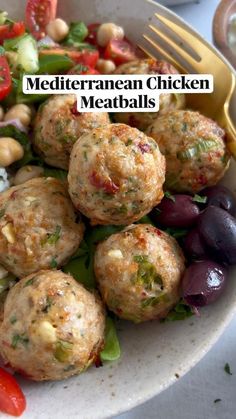 a white plate topped with meatballs next to a fork and salad on top of a table