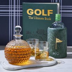 a bottle of golf next to two glasses on a tray with a book in the background