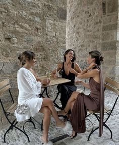 three women sitting at a table talking to each other in an old stone walled building