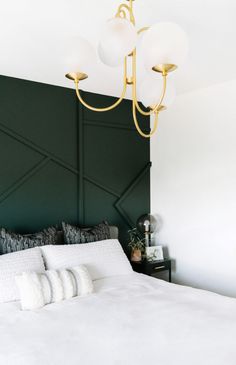 a white bed sitting under a chandelier next to a dark green headboard