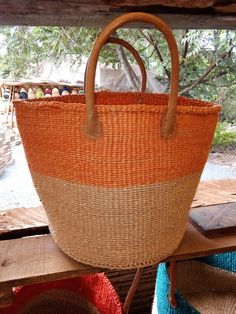 This is an African Sisal and Leather handbag or Planter Handmade in Kenya. It's made from Sisal Fibers and dyed in using natural dyes. It can be made with or without the leather handles depending on preference and use. Planters usually have the leather handles. It is used as a carry on handbag for your laptop, books or for clothes for an overnight stay.  Larger ones can be used for organizing your living room as storage for shawls or books. Larger ones can also be used as laundry baskets. They c Eco-friendly Orange Beach Bag For Daily Use, Eco-friendly Orange Beach Bag For Travel, Handmade Orange Bags With Double Handle, Leather Handle Bucket Bag For Market, Orange Tote Bag For Market, Orange Bucket Bag, Handwoven Orange Tote Beach Bag, Orange Handwoven Tote Beach Bag, Handwoven Orange Beach Bag