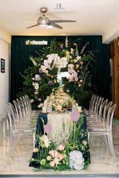 the table is set up with clear chairs and floral centerpieces, along with greenery