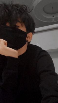 a young man wearing a black mask covering his face with one hand and looking at the camera