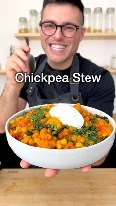 a man holding a white bowl filled with chickpea stew and topped with sour cream