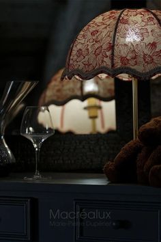 a lamp that is on top of a table next to a wine glass and a teddy bear