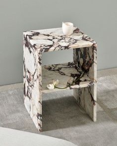 a marbled side table with a white flower on the top and a gray wall in the background