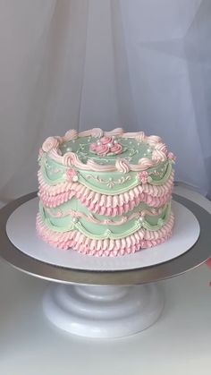 a pink and green cake sitting on top of a silver platter next to a white wall