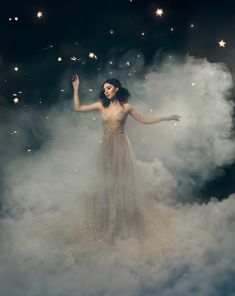 a woman standing in the clouds with her arms outstretched and hands out, surrounded by stars