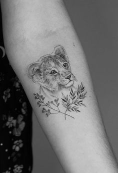 a small lion tattoo on the left forearm and arm, with leaves in front of it