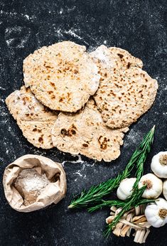 garlic bread and garlic on a black surface next to garlic, herbs and an egg shell