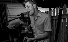 a man singing into a microphone while holding an acoustic guitar