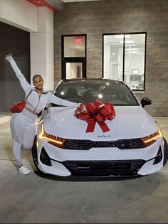 a woman standing next to a white car with a red bow on it