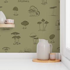 a green wall with mushrooms on it and a white vase next to the shelf in front