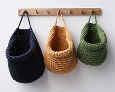 three crocheted baskets hanging on a wall with wooden pegs attached to them