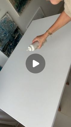 a woman is using a spray bottle to paint a table